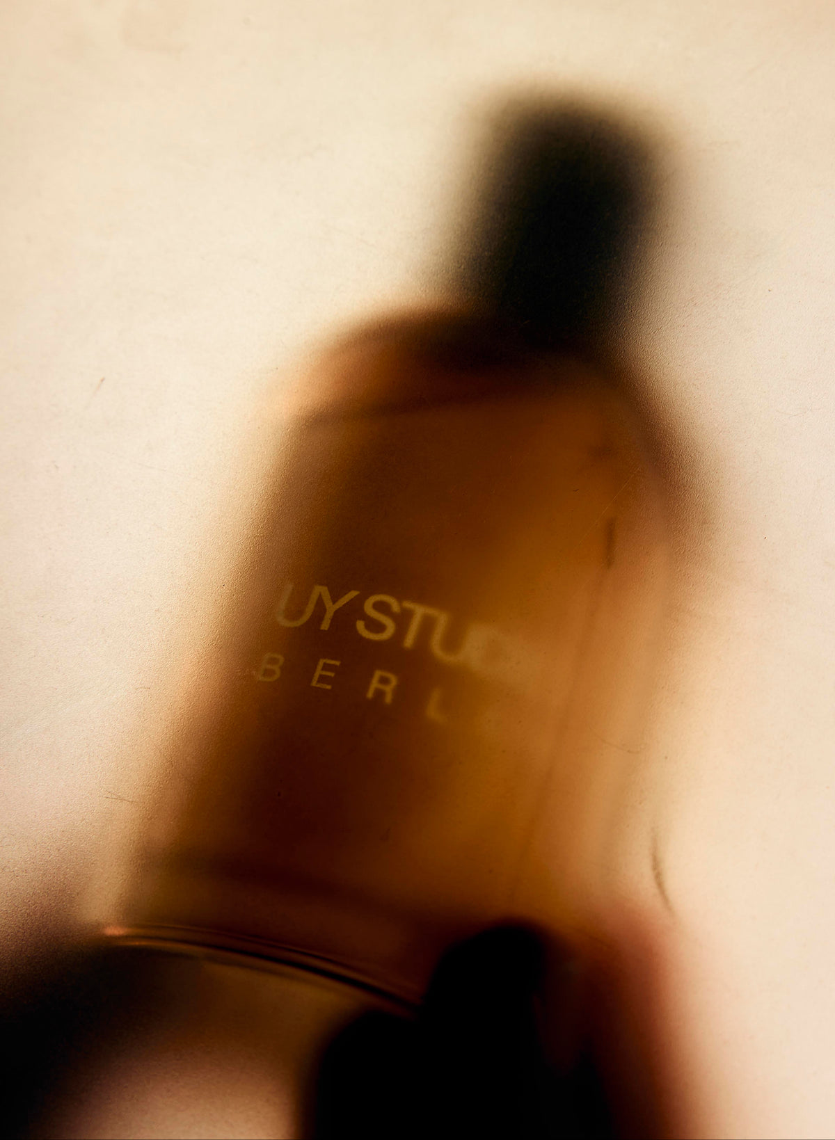 Soft-focus close-up of an amber UY Studio fragrance bottle in warm golden light.